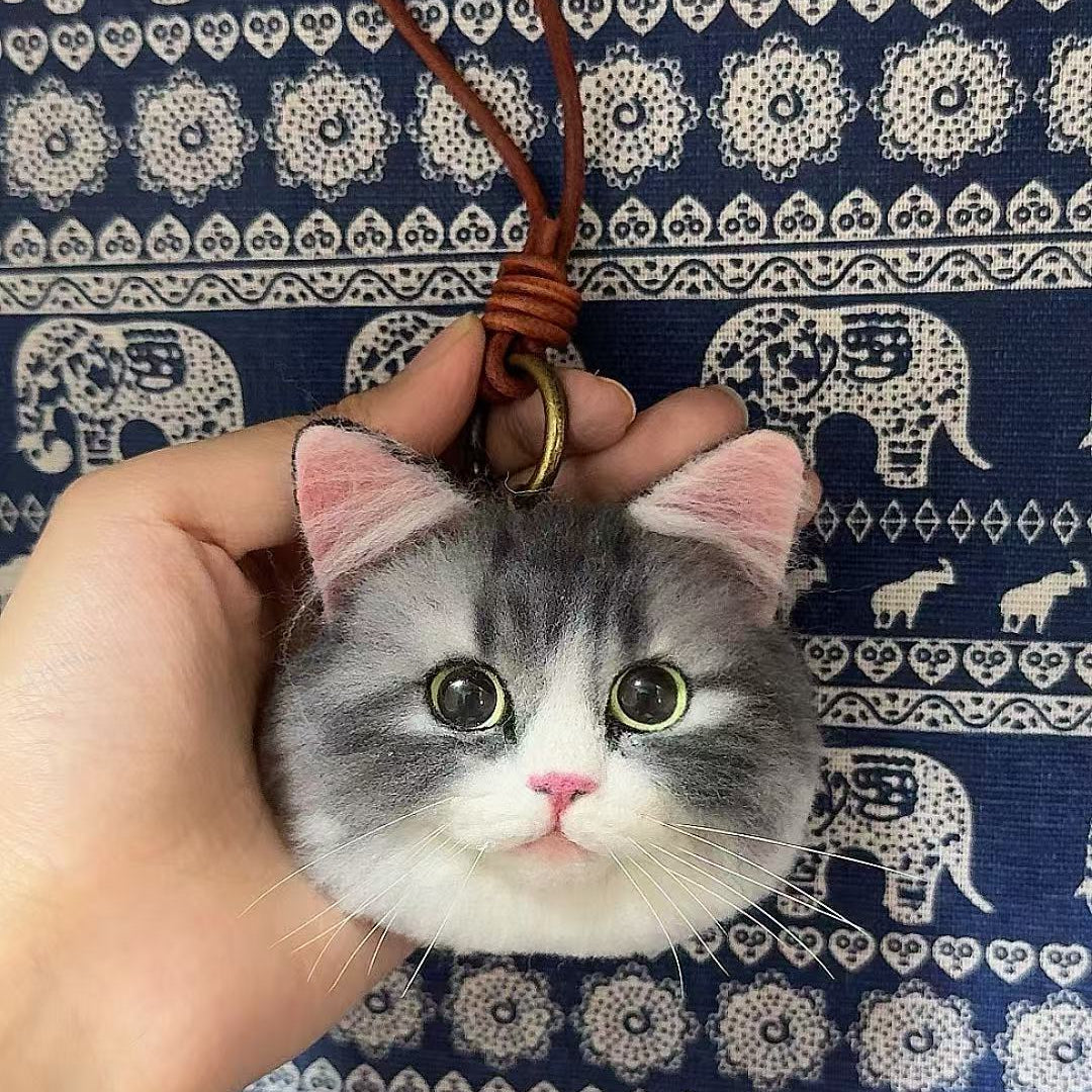 Cat-shaped keychain held by a hand against a blue fabric background with elephant pattern
